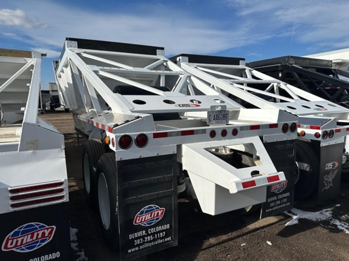 Bottom dump trailer side and rear showing white frame, dual axles, and utility logo plate.