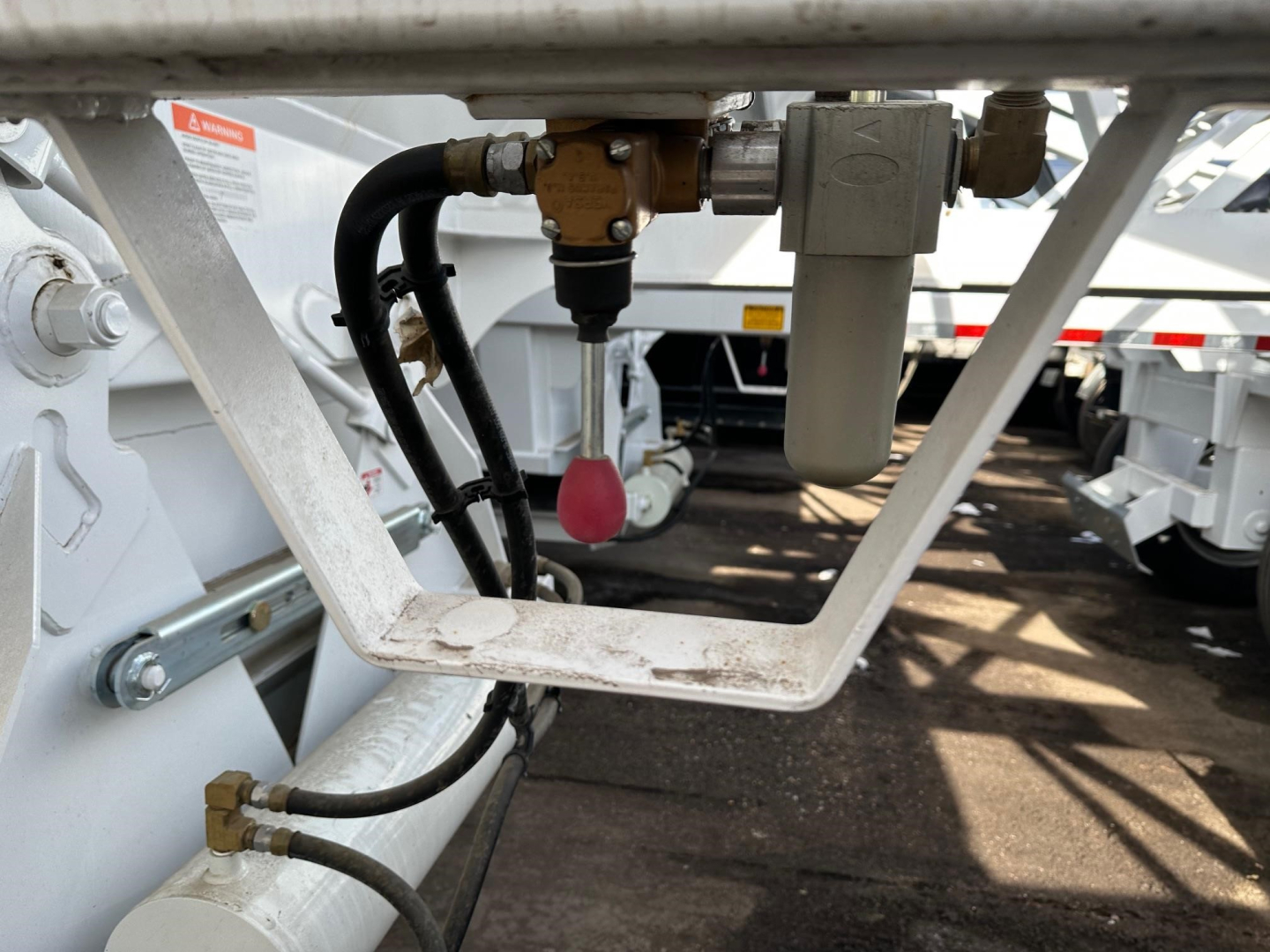 Trailer underside showing hydraulic lines and valve with pink handle, fitting, and aluminum frame of a 40' air ride bottom dump trailer.