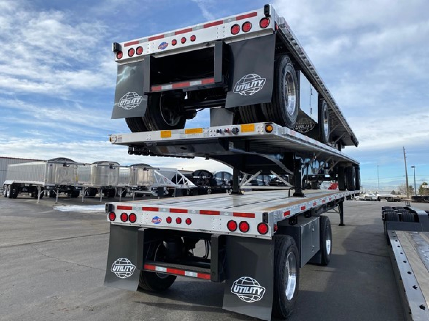 New Utility 4000Ae flatbed trailer stacked on another trailer showing dual tandem axles and spare tires with Utility logos.