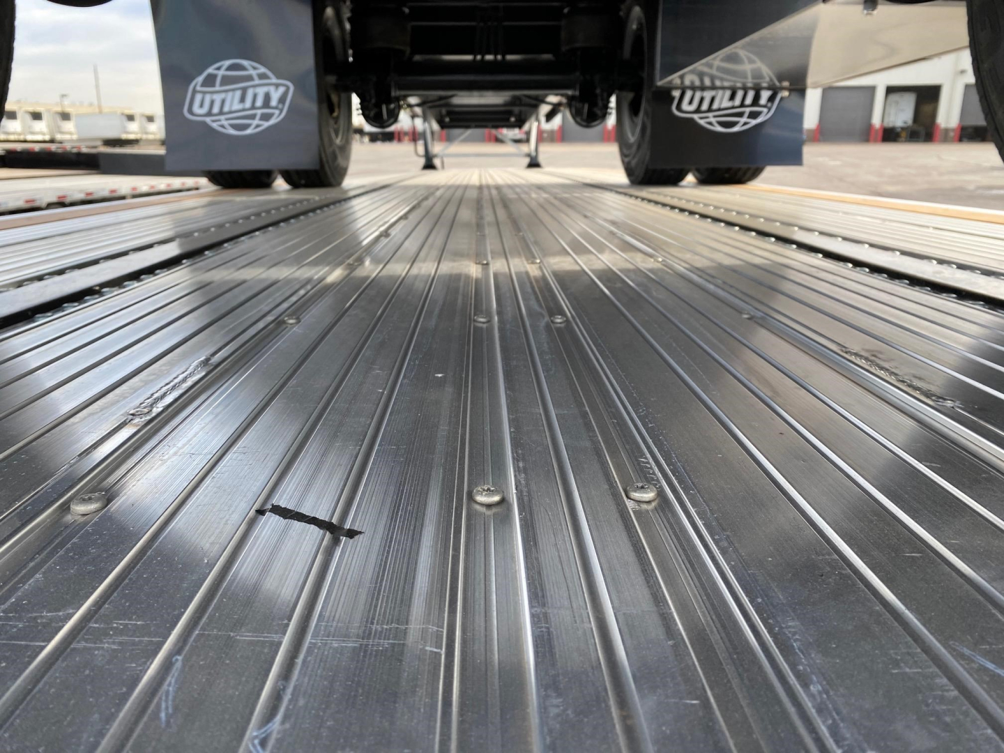 Utility 4000Ae flatbed trailer deck looking down from axle level, shiny ribbed steel surface, undercarriage and wheels visible in background.