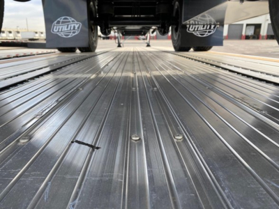 Utility 4000AE flatbed trailer deck showing corrugated steel surface and undercarriage with fender skirts and branding.