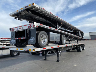 Trailer flatbed with a raised utility 4000Ae trailer, showing wheels, undercarriage, and support posts; spare tire and fender visible; loading ramps and reflective tape along edges.