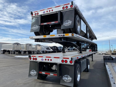 New Utility 4000Ae flatbed trailer stacked on another trailer showing dual tandem axles and spare tires with Utility logos.