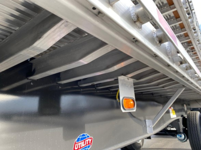 Utility 4000Ae flatbed trailer underside showing frame, side rail, and a small rectangular clearance light with orange lens; wheel and hitch area partially visible.