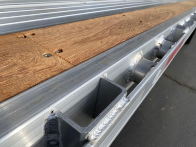 Trailer bed edge with wooden plank and side rail, view of aluminum frame and riveted brackets along the edge.