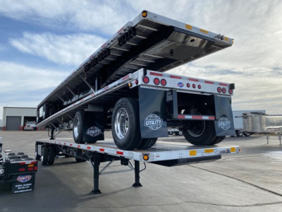 Flatbed trailer with raised ramp sections showing undercarriage and dual rear axles, Utility brand mud flaps, and rear lights.