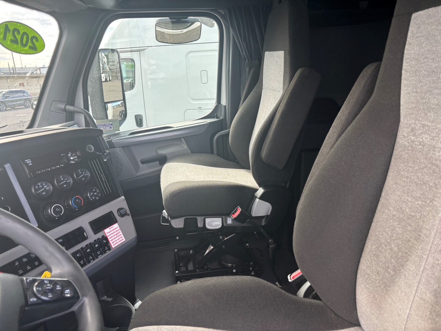 Trucking cab interior of a Freightliner CA-126 with driver and passenger seats, dashboard gauges, steering wheel, and a view through the left door window.