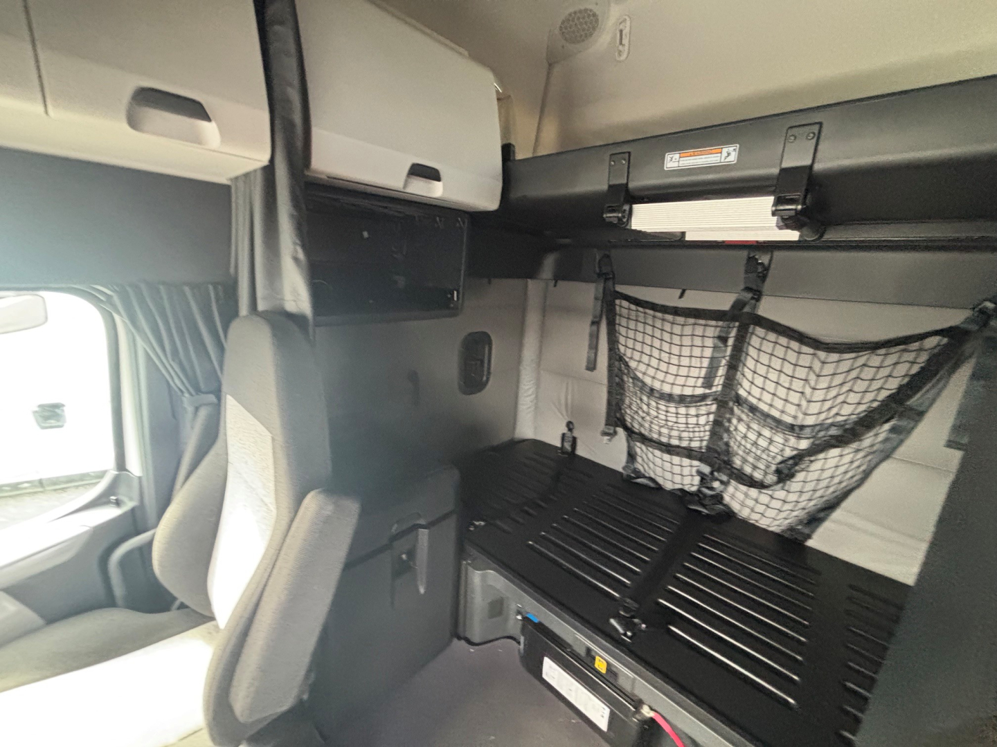 Freightliner truck cab interior showing bunk area with overhead storage and cargo net, cabin wall panels, and bed base.