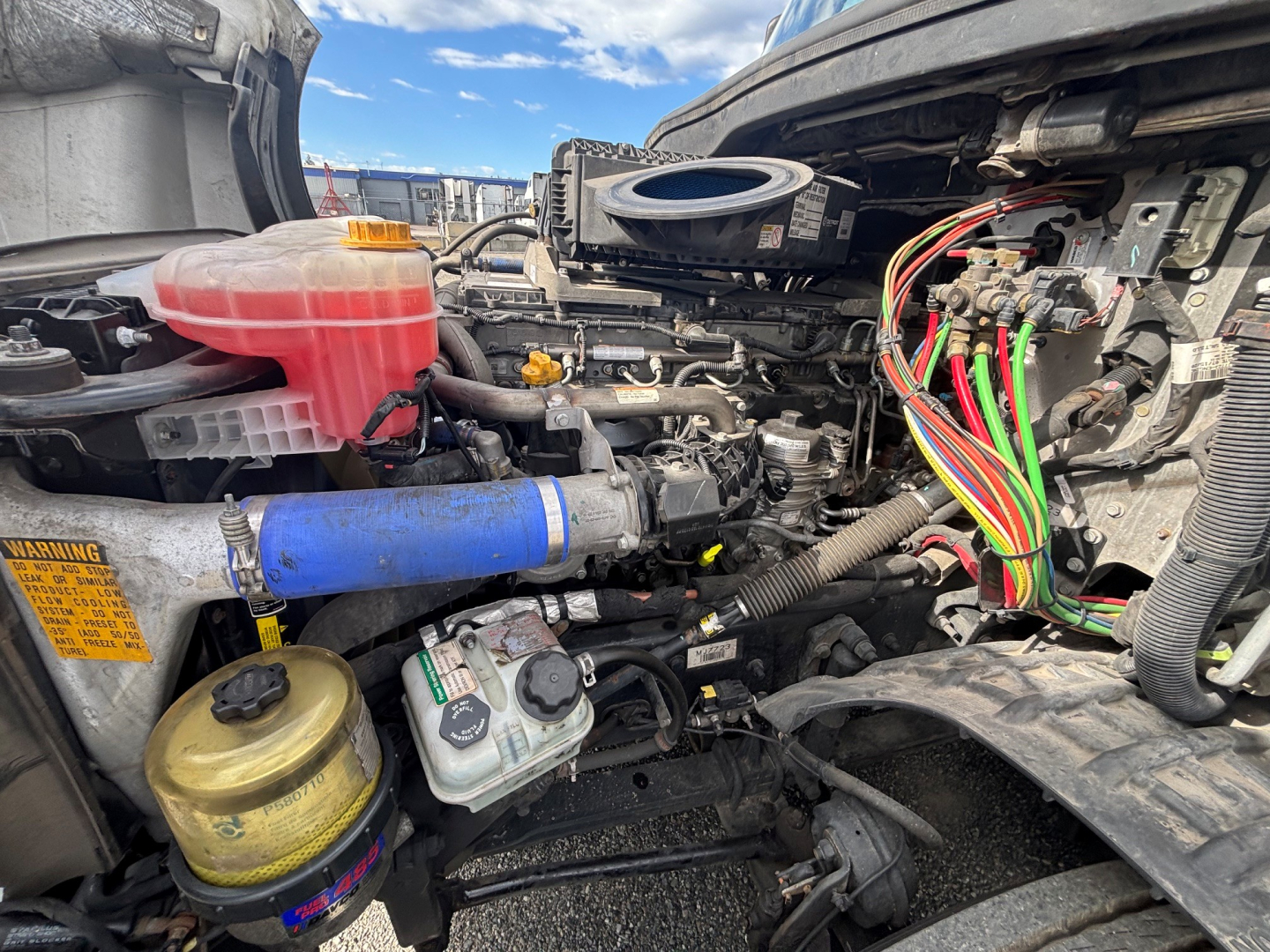 Truck engine bay of a 2021 Freightliner CA-126 showing reservoir bottles, wiring harnesses, hoses, and coolant/air intake components.