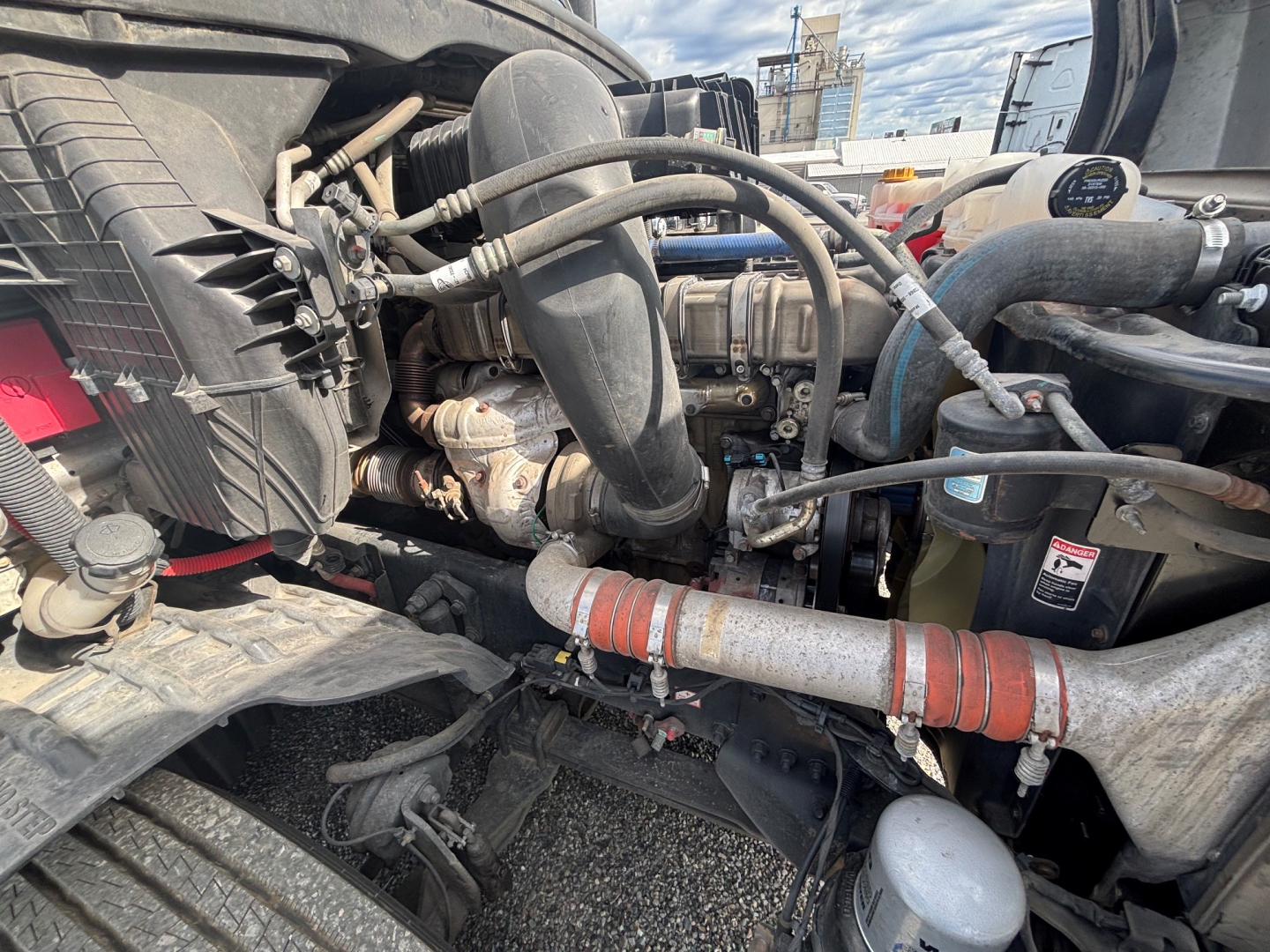 Truck engine bay of a 2021 Freightliner CA-126 showing hoses, coolant lines, air intake, and various engine components.