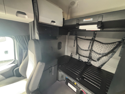 Freightliner truck cab interior showing bunk area with overhead storage and cargo net, cabin wall panels, and bed base.