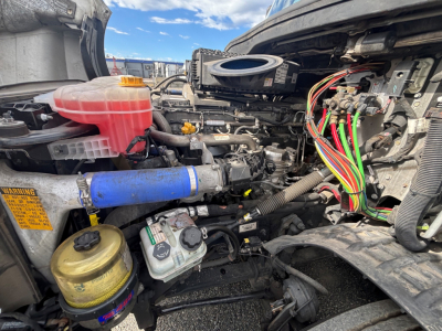 Truck engine bay of a 2021 Freightliner CA-126 showing reservoir bottles, wiring harnesses, hoses, and coolant/air intake components.