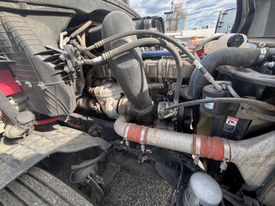 Truck engine bay of a 2021 Freightliner CA-126 showing hoses, coolant lines, air intake, and various engine components.