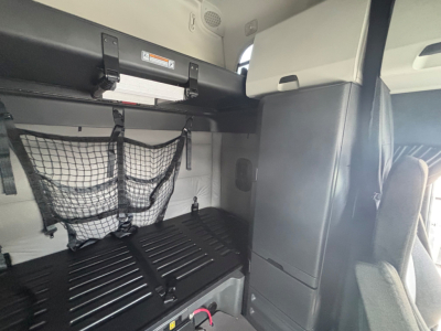 Interior sleeper cab storage area of a Freightliner CA-126 tractor showing a netted cargo pocket, overhead bunk area, and side storage cabinet.