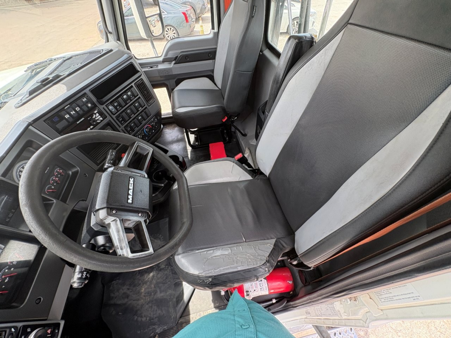 Cab interior of a 2020 Mack PI64T conventional daycab showing steering wheel with Mack badge, gauge cluster, and driver seat; interior materials in black and gray.