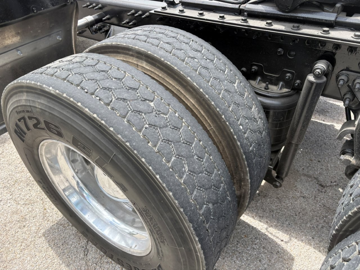 Mack PI64T truck rear dual tires with tread and wheel visible, undercarriage and suspension components partially visible.