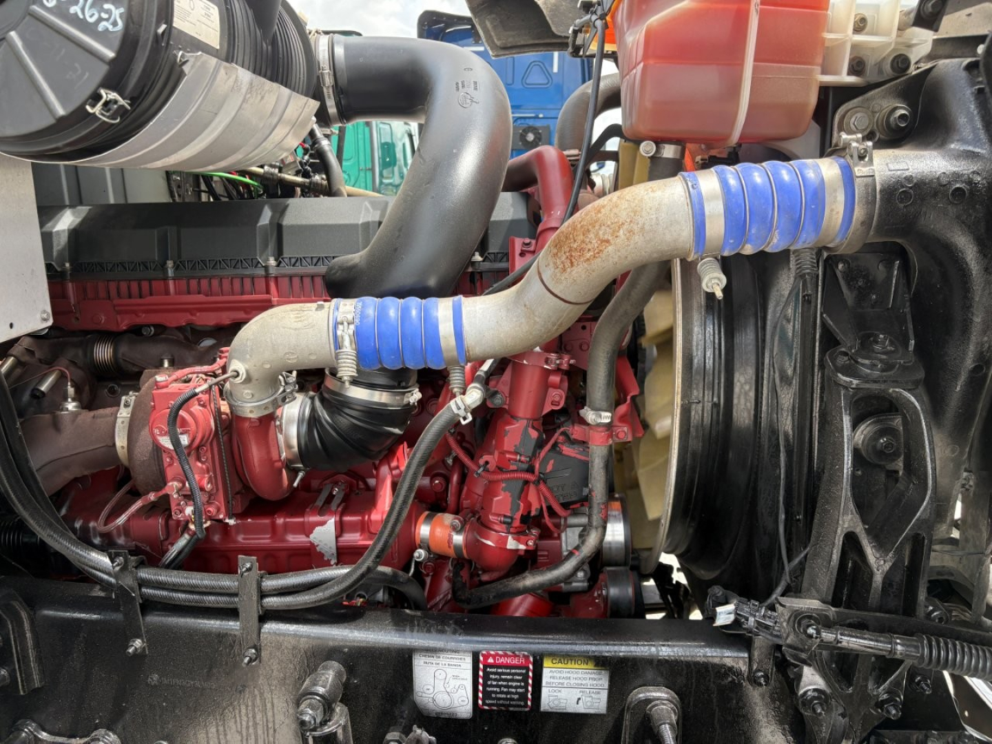 Mack PI64T engine bay showing turbo hoses, red engine block, blue silicone intercooler hoses, coolant reservoir, and radiator.