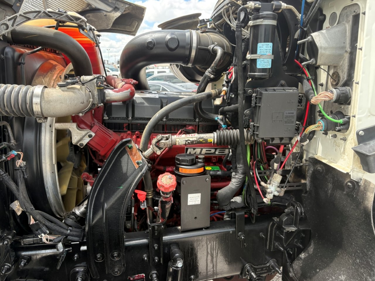 Engine bay of a 2020 Mack PI64T conventional daycab showing turbocharger, intercooler hoses, air intake, batteries, wiring, and label on a blue component.
