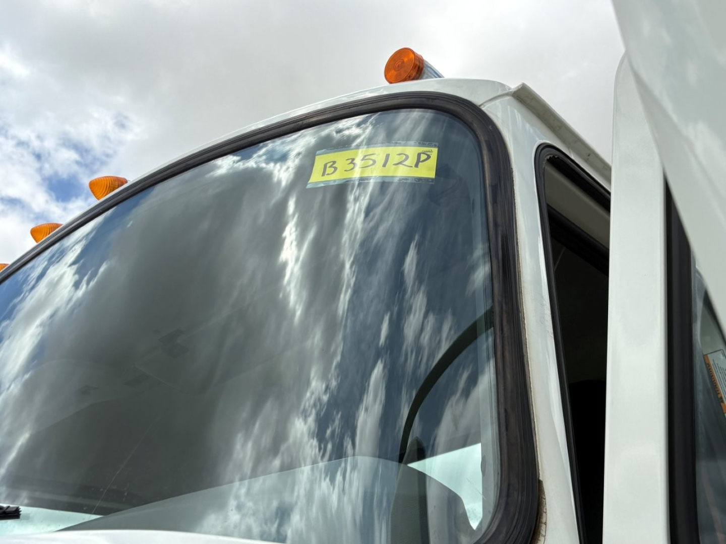 Cab/front corner of a 2020 Mack PI64T conventional daycab showing a yellow stock tag B3512P on the windshield with orange clearance lights