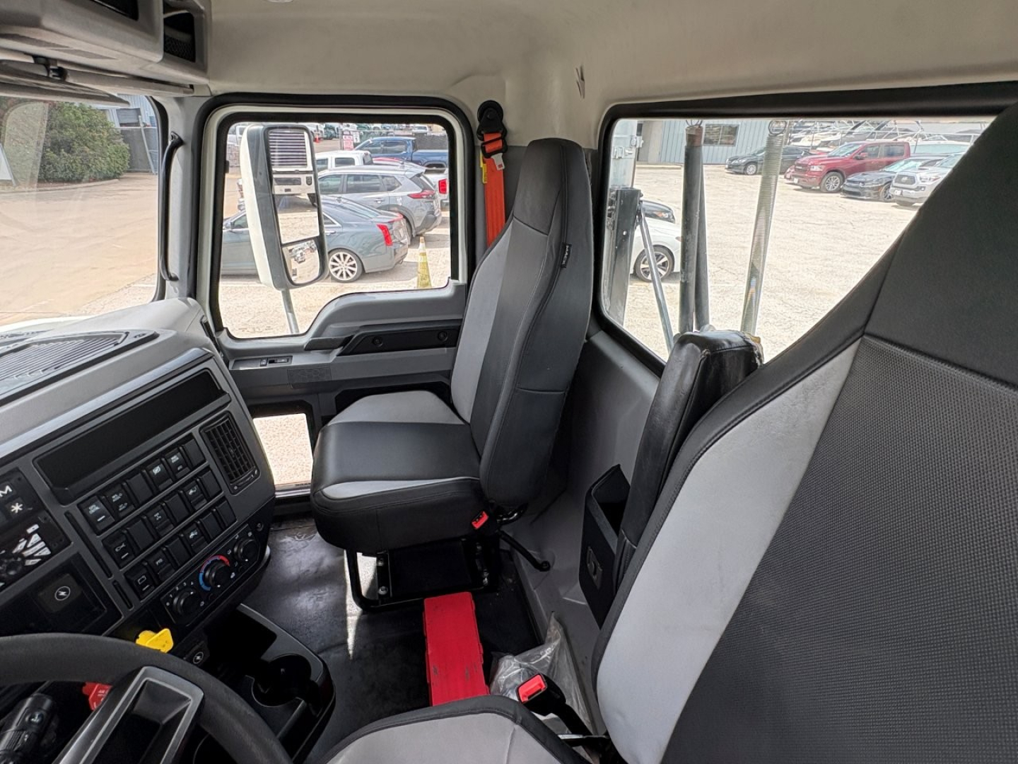 Truck cab interior showing driver seat, passenger seat, dashboard with controls, steering wheel, and window views.