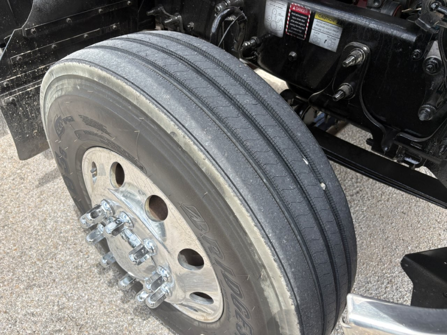 Mack PI64T left front wheel and suspension showing dual rear axle hub area with tire tread and wheel bolts.