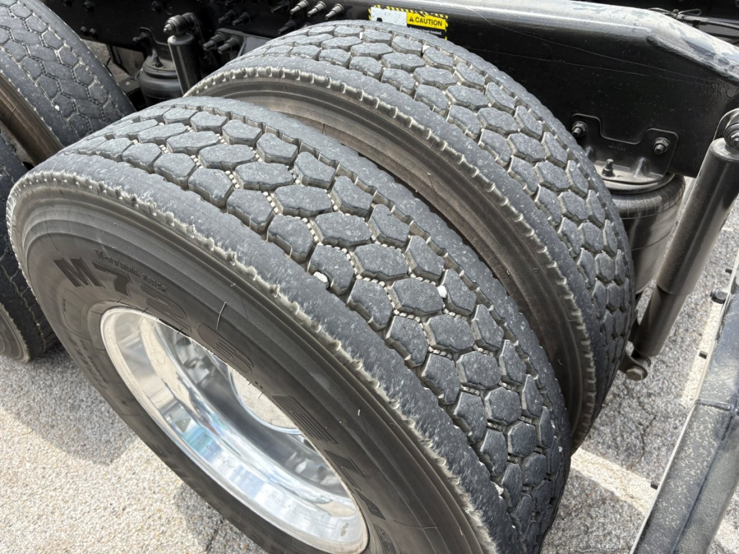 Mack PI64T truck dual rear wheels with heavy-duty tires and drivetrain area visible. Includes portion of chassis and cabin mounting, with tread pattern clearly shown.