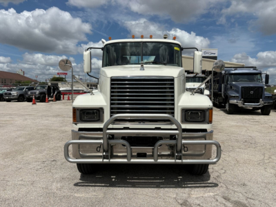 Front view of a white 2020 Mack PI64T cab-over truck with a large grille and a heavy-duty bumper guard. Visible are dual rectangular headlights, a chrome bumper with a tubular grille guard, and amber clearance lights on the cab top.