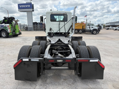 Rear view of a white 2020 Mack PI64T daycab on a truck lot, showing dual rear axles and black mud flaps, with a Volvo dealership in the background.