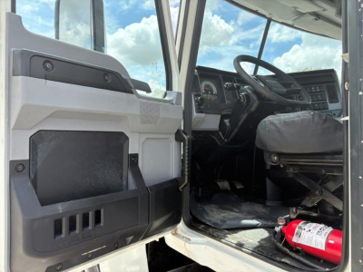 Truck cab interior visible from open driver door showing dashboard, steering wheel, and floor area with a fire extinguisher; partial exterior door panel and step.