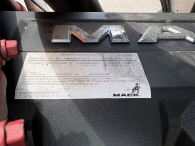 MACK PI64T engine bay badge area with large 'MACK' lettering and a metal identification plate containing text labels.