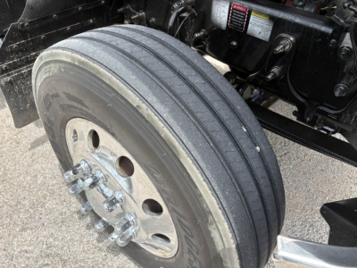 Mack PI64T left front wheel and suspension showing dual rear axle hub area with tire tread and wheel bolts.