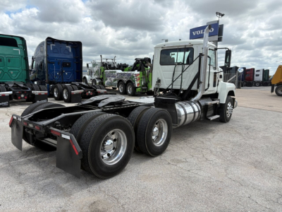 Mack PI64T conventional daycab tractor rear and side view showing dual rear axles, fuel tanks, exhaust stack, and white cab.
