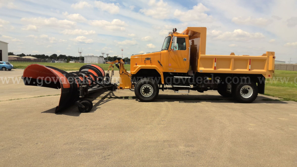 Volvo Autocar dump truck with plow attachment on front, orange cab and bed, side view, VIN 4VHSALRH7VR517740 visible