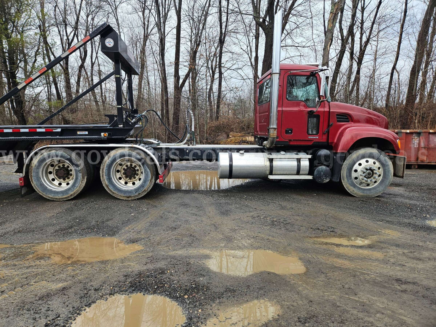 Mack CV713 Granite truck showing side view with red cab and black trailer hitch, fuel tanks, and wheels.