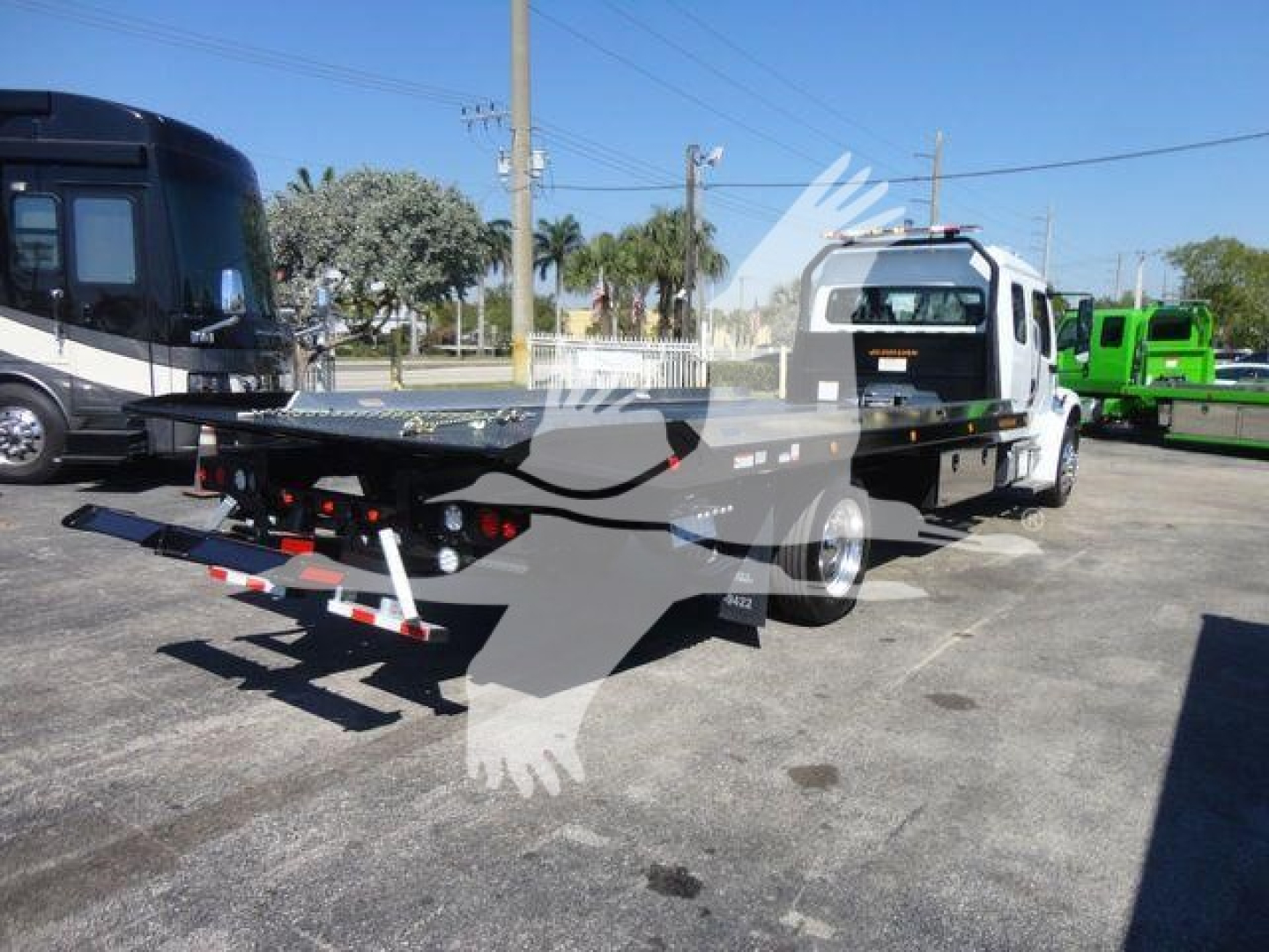 Flatbed tow truck in a dealership lot showing a Freightliner M2 106 with rollback bed and attached tow equipment.