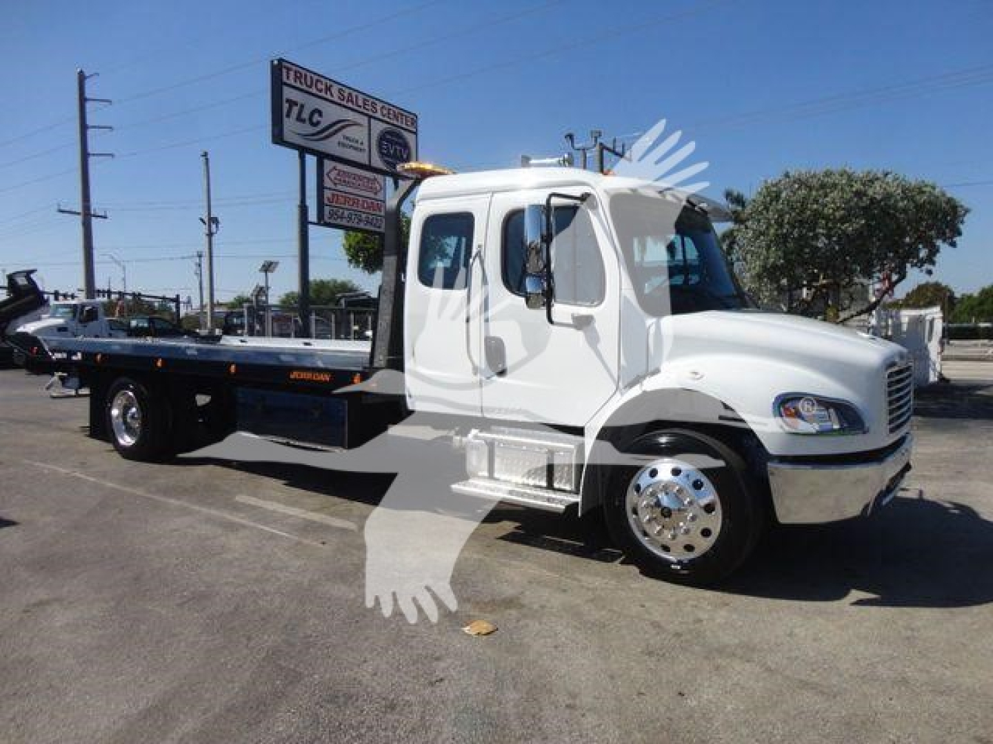 Freightliner M2 106 rollback truck in white cab with flatbed, side view showing cab and front wheels, dealership lot in background.
