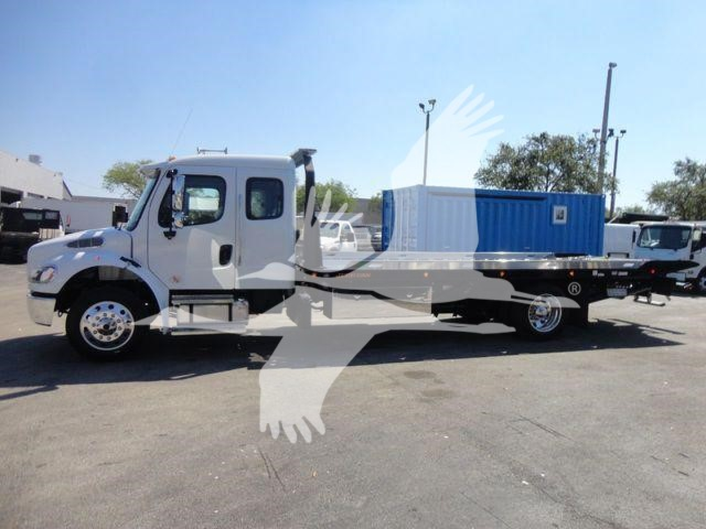 Freightliner M2 106 rollback truck in side view with a flatbed and blue equipment container in the bed.
