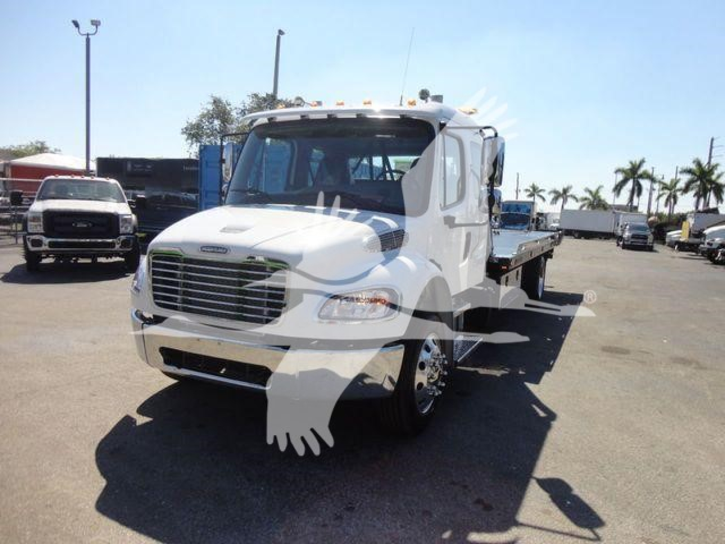 Freightliner M2 106 rollback truck front-left view showing cab, grille, headlights, and flatbed/roll-back chassis.