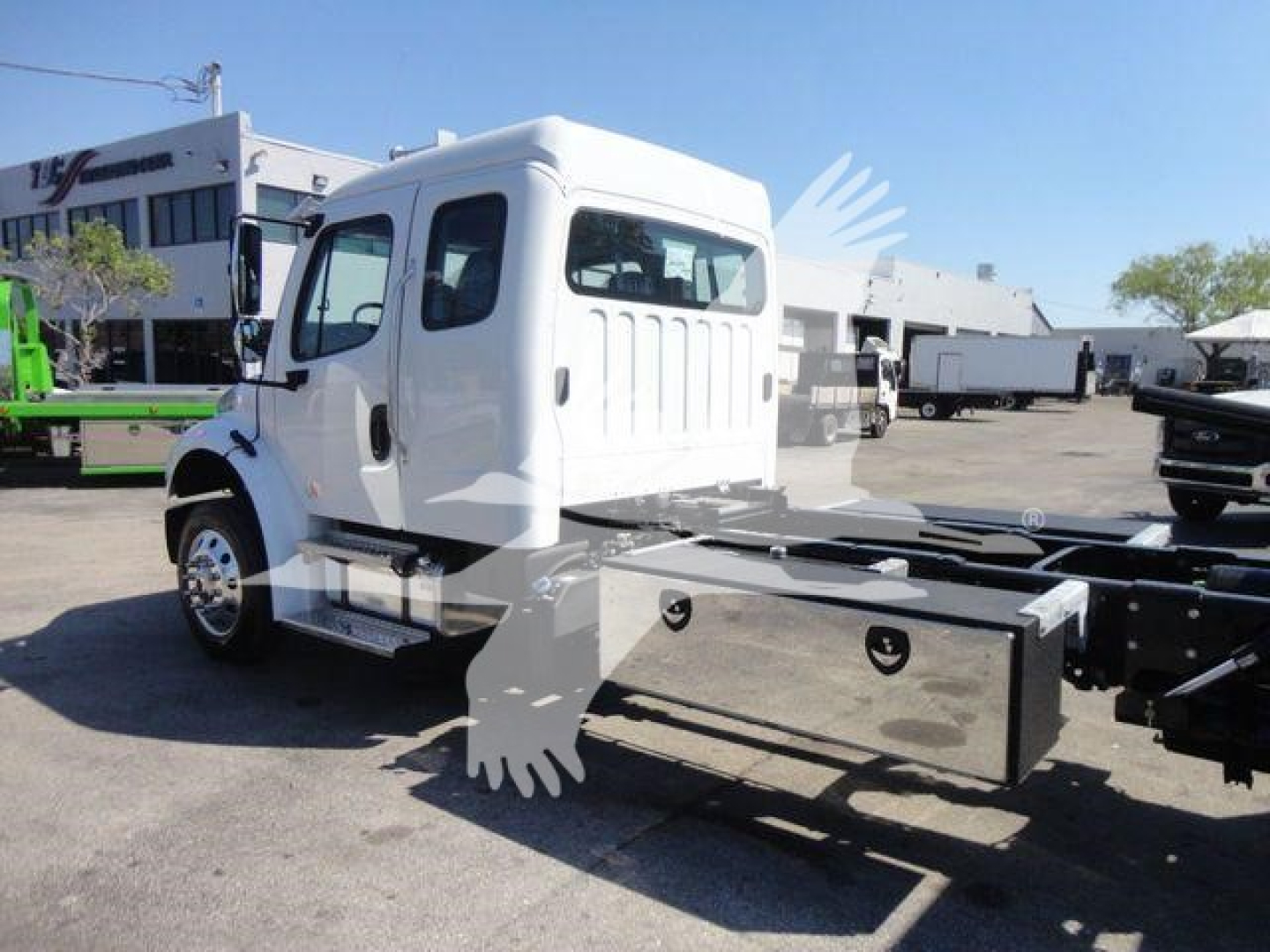 Truck cab of a white Freightliner M2 106 with a large front fuel/tool box, attached to a rollback chassis. The image shows the driver cab, entry steps, and side windows.