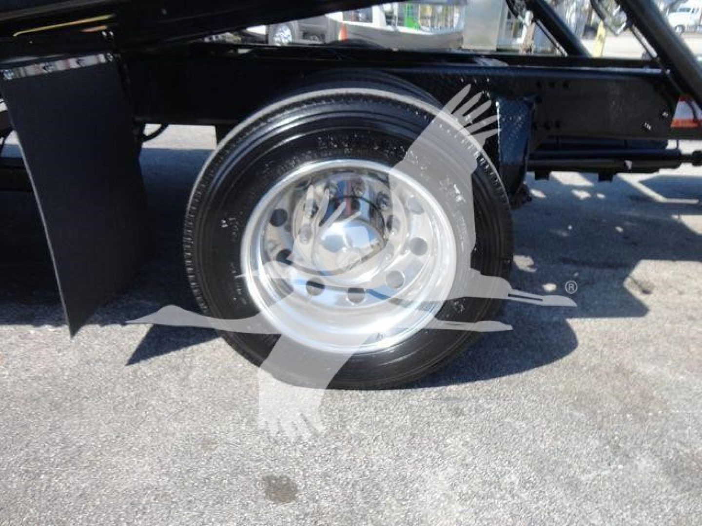 Wheel and suspension area of a Freightliner M2 106 rollback truck showing a polished steel wheel, tire, and part of the undercarriage.