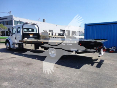 Freightliner M2 106 rollback truck with flatbed and wheel lift in a dealership lot, side view showing cab and flatbed equipment.