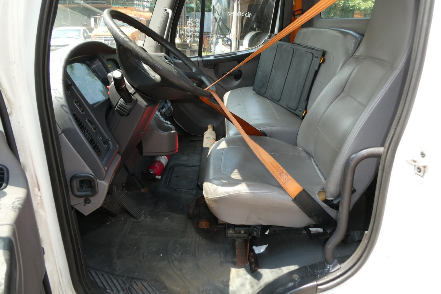 Truck cab interior of a 2008 Freightliner M2-106 with grey seats and orange seat belt, steering wheel, dashboard, and floor mat visible.