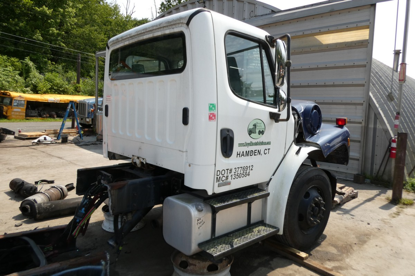 Truck cab side view with white sleeper and Freightliner M2-106 tag, VIN plate and service decals visible.