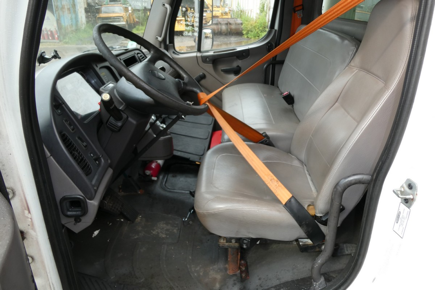 Cab interior of a 2008 Freightliner M2-106 showing grey vinyl seats, steering wheel, dashboard, and orange seat belt across the front seat.