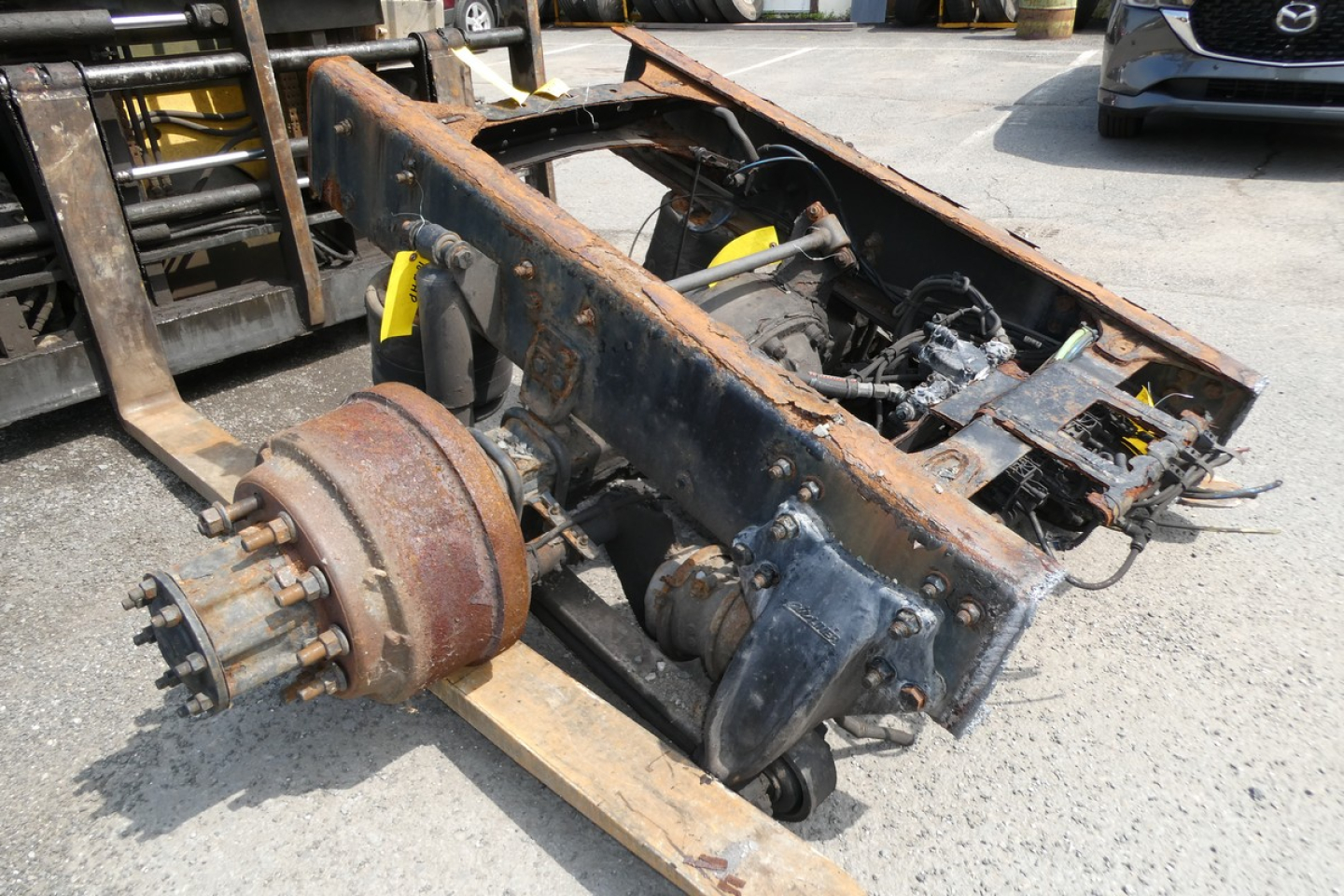 Front view of a rusty, removed Freightliner M2-106 chassis frame with drivetrain components exposed, including a drive hub and axle assembly.