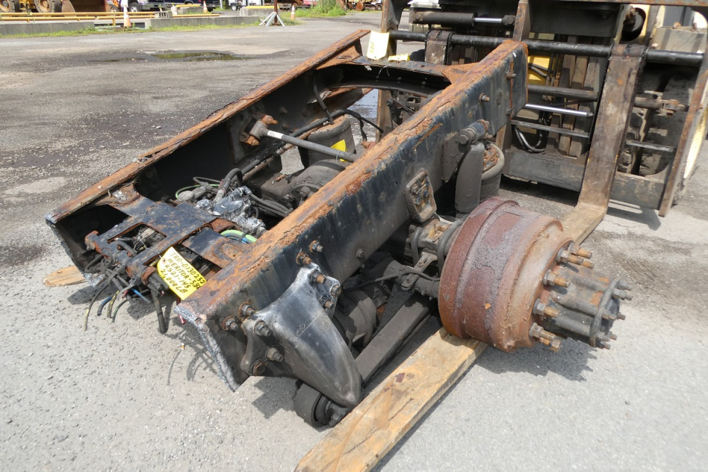 Freightliner M2-106 chassis frame and rear axle assembly with rusted drum hub and exposed wiring, viewed from side on ground.