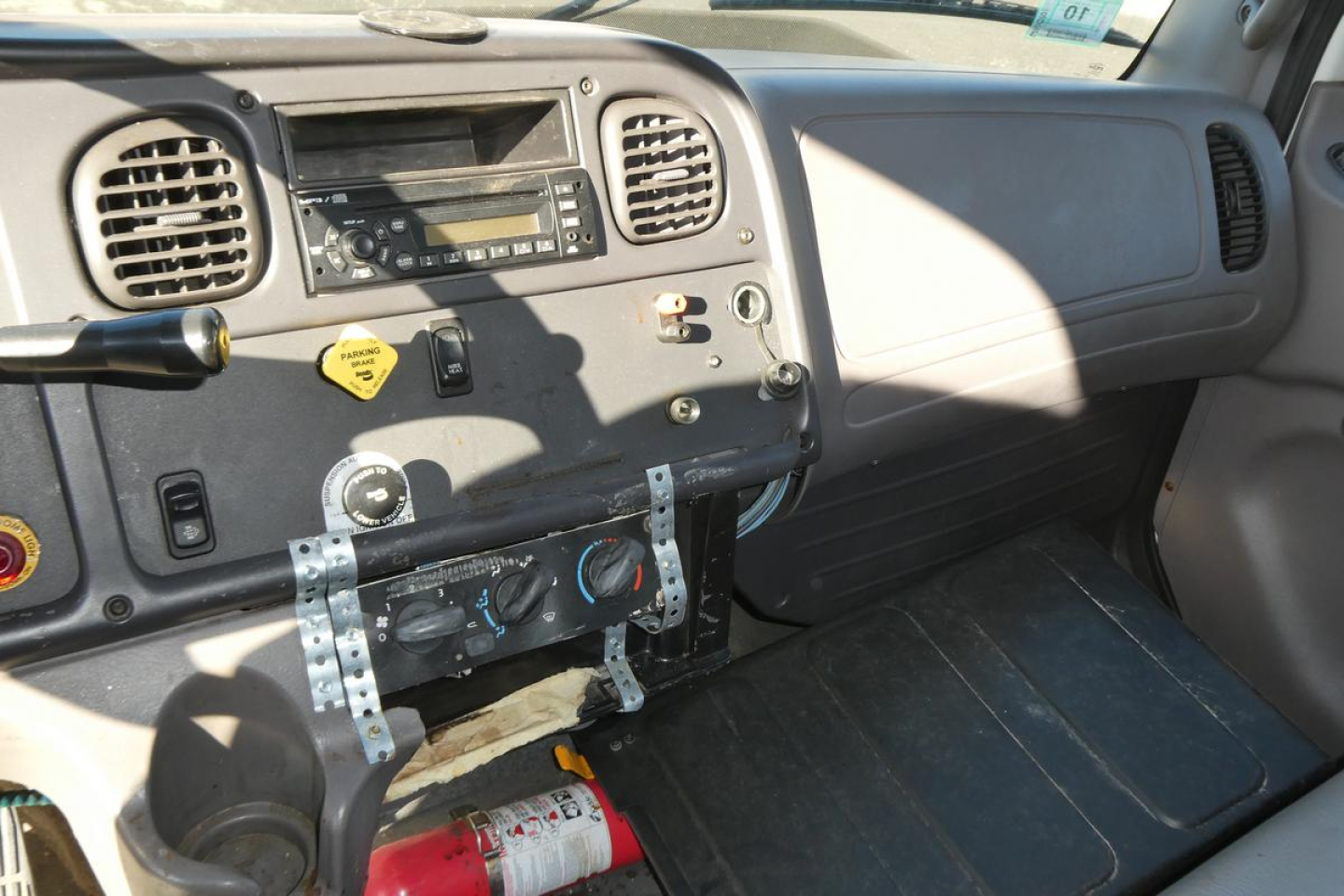 Dashboard and center console of a Freightliner M2-106 cab with radio, control switches, and levers visible; fire extinguisher near floor.
