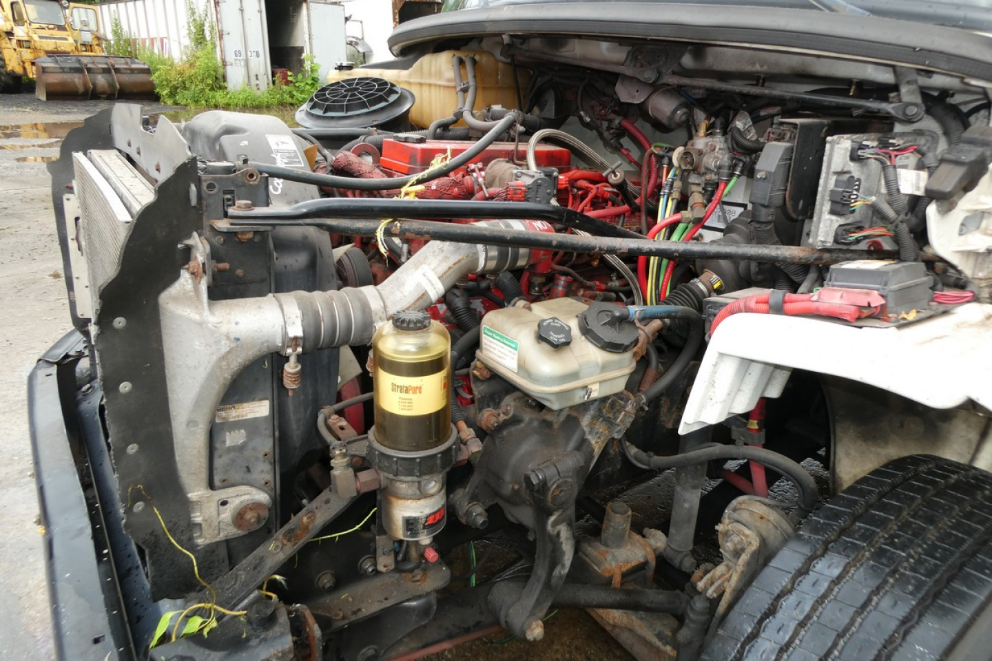 Freightliner M2-106 engine bay showing assorted hoses, wiring, and a fuel filter canister near the front left side.