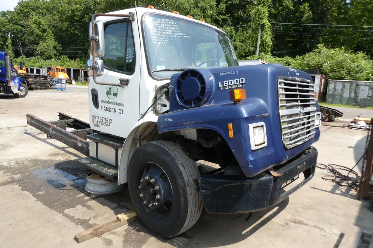 Used 2008 Freightliner M2-106 box truck with damaged fender and missing front wheel; front grille, L8000 label on blue hood; passenger side shows white cab with Han-dben CT logo and text; VIN sticker not visible; stock number 0130252 visibl