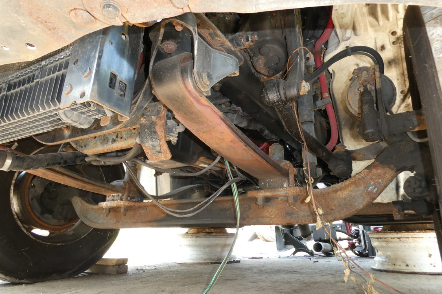 Underbody view of a 2008 Freightliner M2-106 truck chassis showing exhaust pipe, frame, and wiring harness with some rust and components.